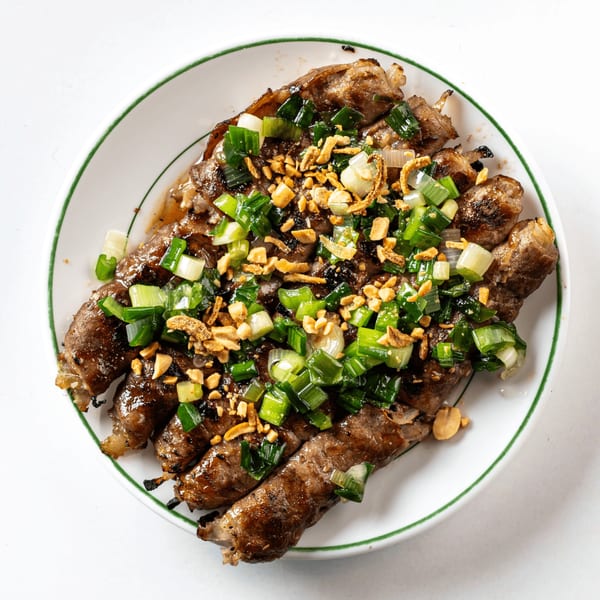 Grilled beef rolls topped with chopped green onions, fried shallots, and peanuts on a white plate.