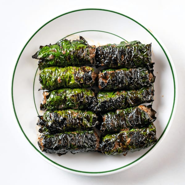 Grilled Vietnamese wild betel leaf-wrapped beef (Bò Lá Lốt) on a white plate with a green rim.