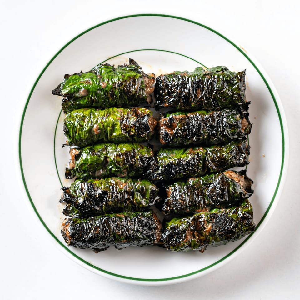 Grilled Vietnamese wild betel leaf-wrapped beef (Bò Lá Lốt) on a white plate with a green rim.