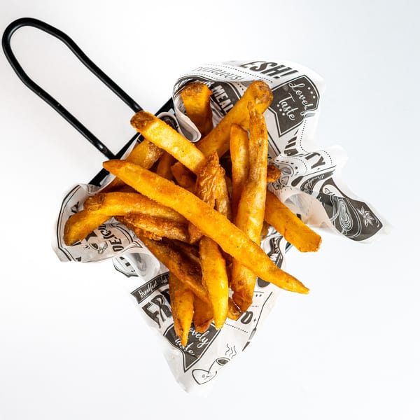 Golden brown french fries in a black wire basket lined with patterned paper, against a white background.