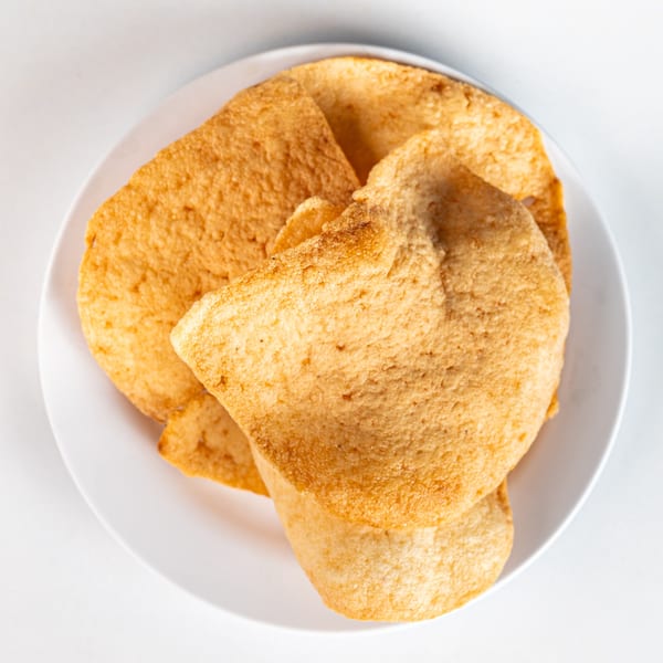 A white plate holds several golden-brown, crispy Vietnamese shrimp chips, also known as Banh Phong Tom.
