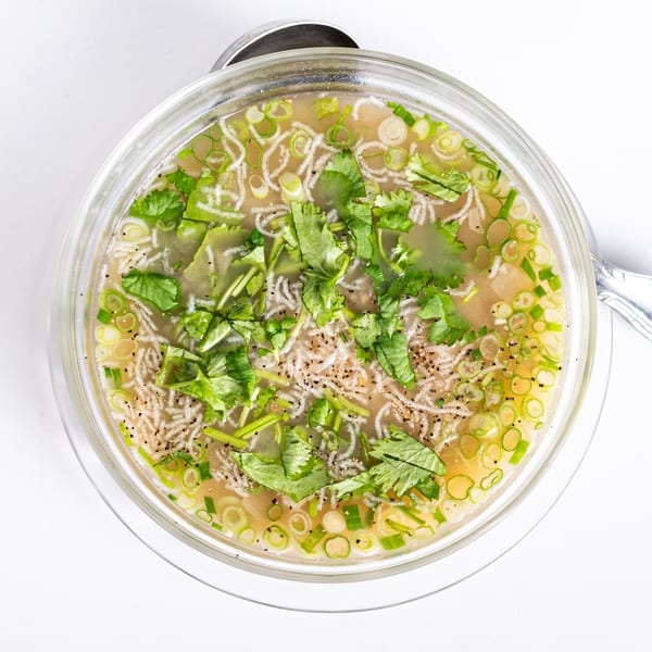 Overhead view of a clear bowl of Vietnamese soup with noodles, cilantro, and green onions.