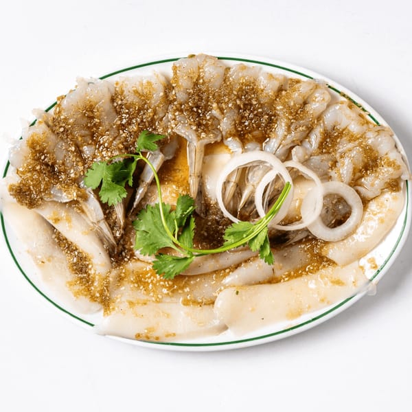 Raw shrimp and squid sashimi with sesame dressing, cilantro, and onion on a white plate.