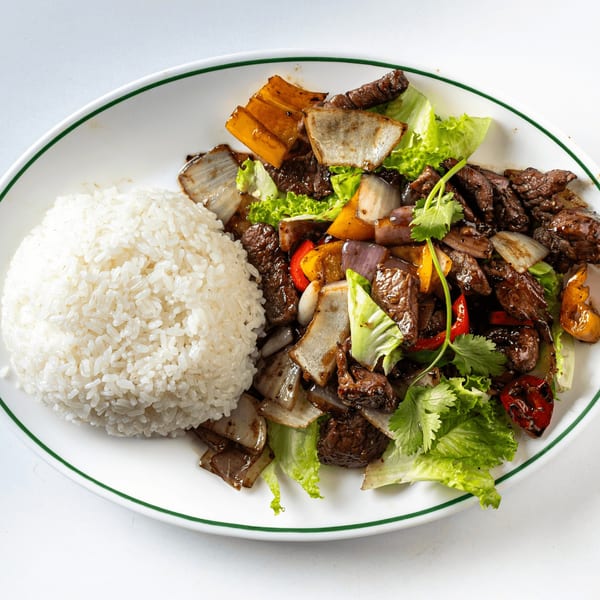 A white plate with a green rim holds a serving of rice and beef stir-fry with vegetables.
