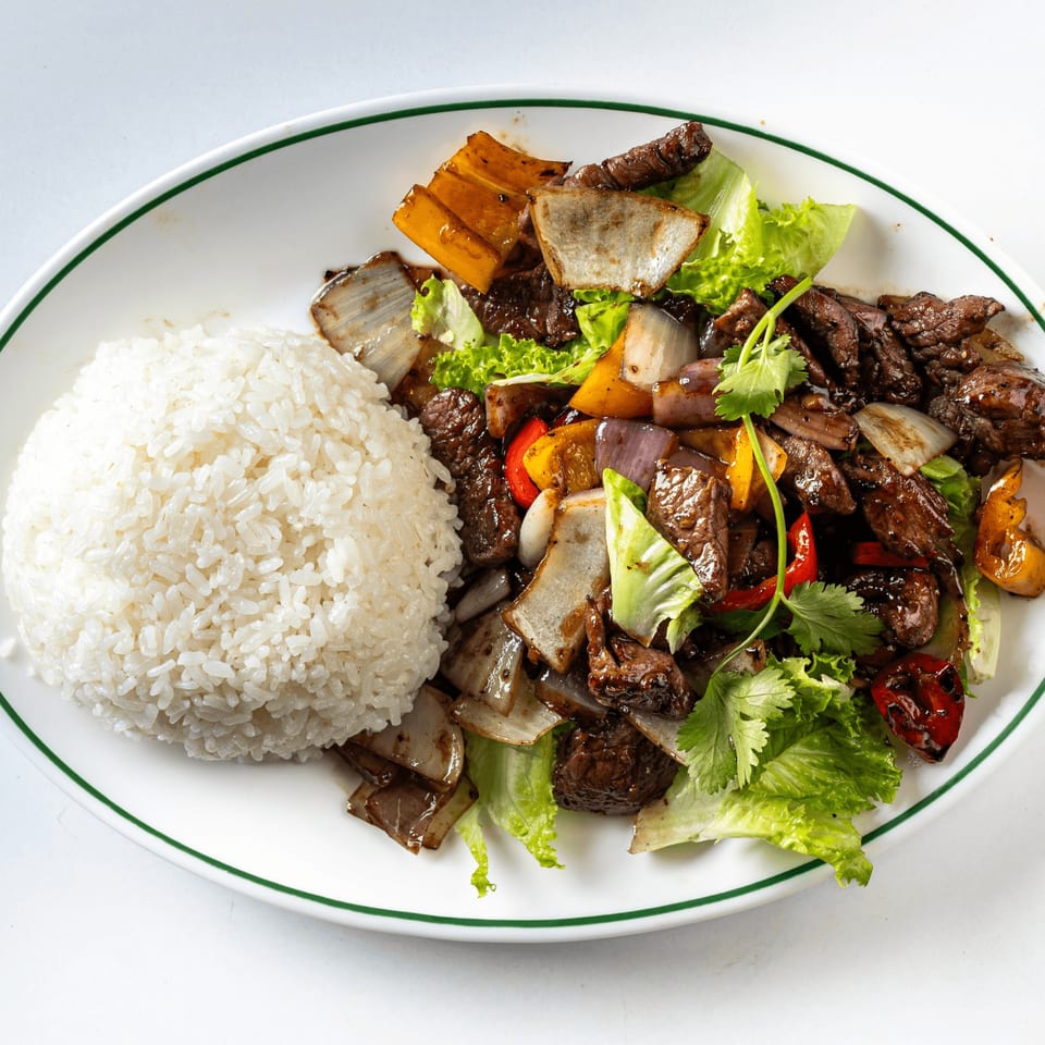 A white plate with a green rim holds a serving of rice and beef stir-fry with vegetables.
